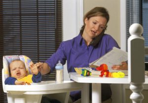Mom working at kitchen table with crying baby in high chair